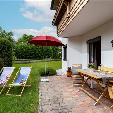 Ein gemütlicher Außenbereich mit zwei Liegestühlen und einem Sonnenschirm. Der Tisch ist für eine entspannte Mahlzeit im Freien gedeckt.
