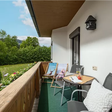 Ein gemütlicher Balkon mit zwei Stühlen und einem kleinen Tisch. Im Hintergrund ist eine grüne Landschaft mit Bäumen zu sehen.