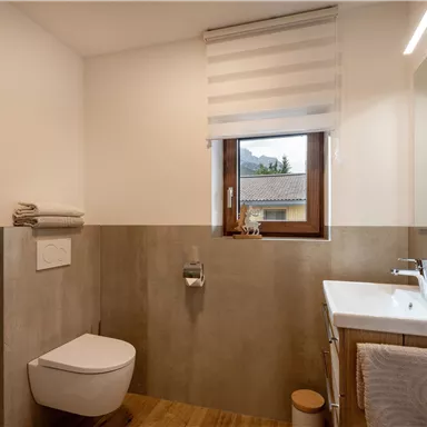 Ein modernes Badezimmer mit Dusche und WC. Helle Farben und große Fenster sorgen für eine freundliche Atmosphäre.
