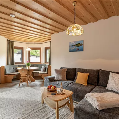 Ein gemütliches Wohnzimmer mit einer modernen Couch und einem Holztisch. Große Fenster sorgen für viel Tageslicht und eine einladende Atmosphäre.