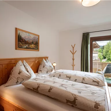 Ein gemütliches Schlafzimmer mit einem Doppelbett und Holzdetails. Große Fenster bieten Blick auf einen grünen Außenbereich.