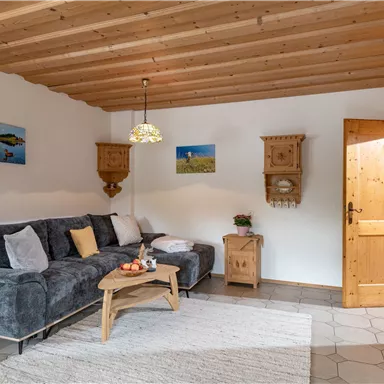Ein gemütliches Wohnzimmer mit einer grauen Couch, einem Holztisch und dekorativen Bildern an der Wand. Die warmen Holzdetails schaffen eine einladende Atmosphäre.