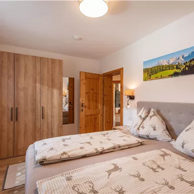 Ein gemütliches Schlafzimmer mit einem Doppelbett und einer Holzkommode. Die Wände sind hell, und ein großes Fenster sorgt für viel Tageslicht.