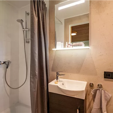 A modern bathroom with a shower niche and a sink. The walls are light and simply designed.
