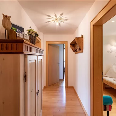 A bright hallway with wooden flooring and a cozy closet. In the background, there is a room with sleeping places and warm light.
