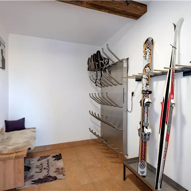 A ski room with skis on a wall mount and space for shoes. There is a seating area and wooden paneling on the wall.