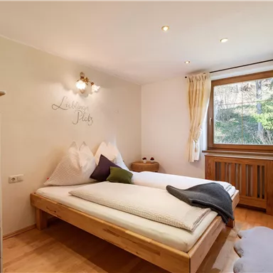 A simple bedroom with a large bed and wooden floor.
There are windows overlooking greenery and a cozy decor.
