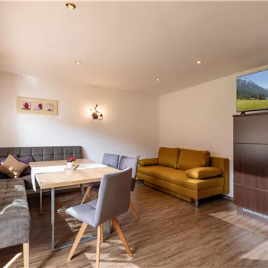 A bright living room with a dining table, a cozy couch, and a television. The rooms are furnished in a modern and inviting way.