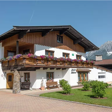 A charming house in alpine style with a large balcony and blooming flowers. Impressive mountains can be seen in the background.