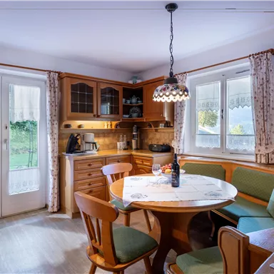 Ein gemütlicher Essbereich mit einem runden Tisch und Holzstühlen. Große Fenster bieten einen Blick auf den Garten draußen.