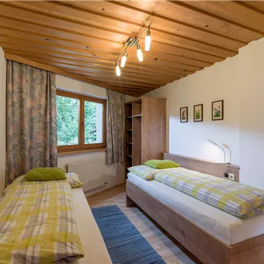 Ein gemütliches Schlafzimmer mit zwei Einzelbetten und Holzdecke. Es gibt Fenster mit Vorhängen und Bilder an der Wand.