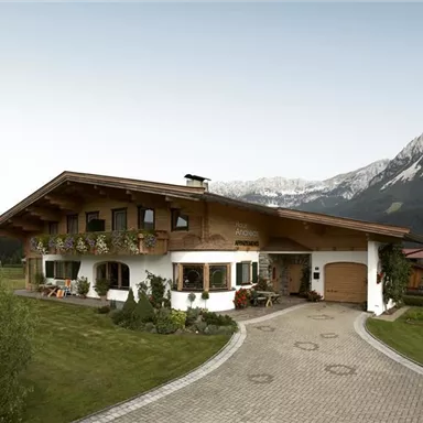 Ein schönes alpenländisches Haus mit Blumenbalkonen. Im Hintergrund sind majestätische Berge zu sehen.