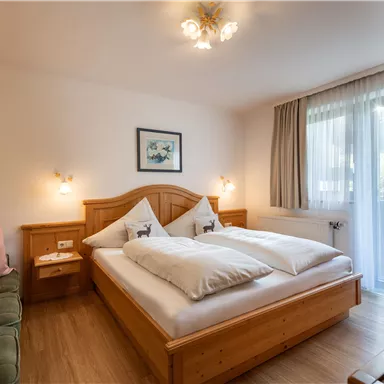 Ein gemütliches Schlafzimmer mit Holz-Möbeln und einem Doppelbett. Große Fenster lassen viel Tageslicht herein und sorgen für eine helle Atmosphäre.