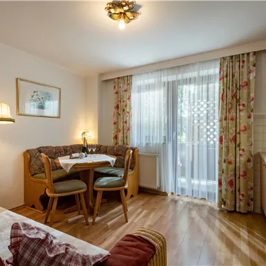 Ein gemütlicher Wohnbereich mit einem Esstisch und Stühlen. Die Küche ist funktional und der Raum hat viel natürliches Licht durch die großen Fenster.