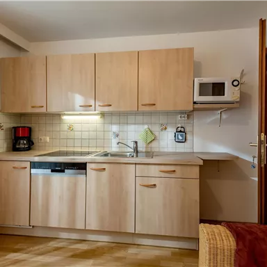 Eine moderne Küche mit hellen Holzschränken und einer Mikrowelle. Auf der Arbeitsfläche sind ein Wasserkocher und eine Kaffeemaschine zu sehen.