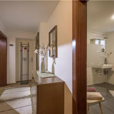 Ein heller und einladender Flur mit einem Holzschrank und modernen Spiegeln. Die Wände sind in einem neutralen Farbton gehalten, und es gibt einen kleinen Waschbereich.