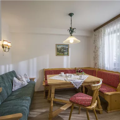 Eine gemütliche Küche mit einem runden Tisch und einer Eckbank. Das Zimmer ist hell und freundlich mit einem Fenster und sanfter Beleuchtung.