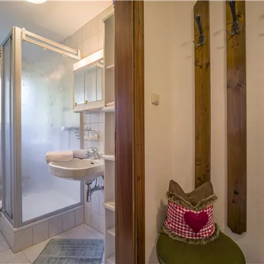 Ein modernes Badezimmer mit einer Dusche, einem Waschbecken und Holzregalen. Die Einrichtung ist hell und freundlich gestaltet.