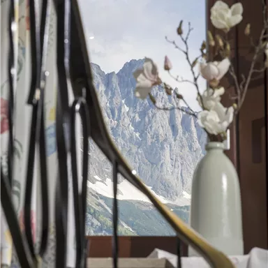 Eine elegante Inneneinrichtung mit einem Blick auf beeindruckende Berge durch ein Fenster. Auf dem Tisch steht eine Vase mit Blumen.