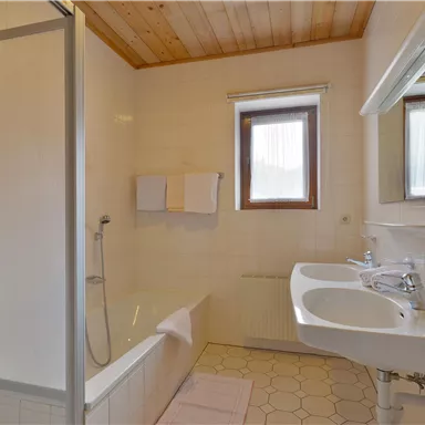 A bright bathroom with a shower and bathtub. White tiles and a window create a friendly atmosphere.