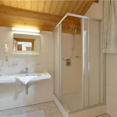 A modern bathroom with a shower and a sink. The wooden ceiling creates a cozy atmosphere.