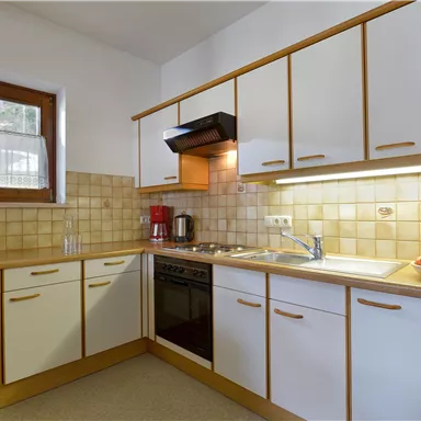 A modern kitchen with white cabinets and wood details. There is a microwave, a stove, and a fruit bowl on the countertop.
