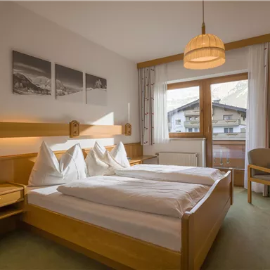 A cozy bedroom with two single beds and wooden furniture. A large window offers a view of the mountains.