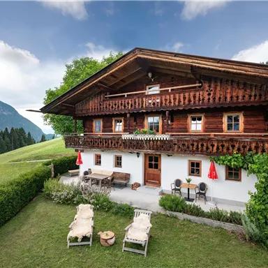 A traditional wooden house in the midst of nature. In the background, green mountains and a blue sky are visible.