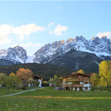A picturesque landscape with majestic mountains and snow-capped peaks. In the foreground, green meadows and traditional houses can be seen.