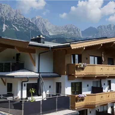 A modern house with wooden cladding in front of an impressive mountain landscape. The sky is clear and the atmosphere is inviting.