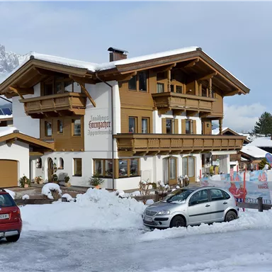 Ein rustikales Gebäude im alpinen Stil, umgeben von Schnee. Vor dem Haus stehen zwei Autos und im Hintergrund sind Berge sichtbar.