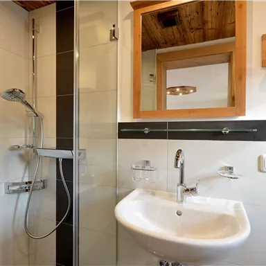 Ein modernes Badezimmer mit Dusche und Waschbecken. Helle Fliesen und Holzverkleidung sorgen für eine freundliche Atmosphäre.