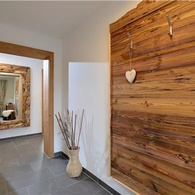 Ein moderner Flur mit einem Holzwandpaneel und stilvollen Dekorationen. Ein Spiegel und eine Vase mit Trockenblumen ergänzen das gemütliche Ambiente.