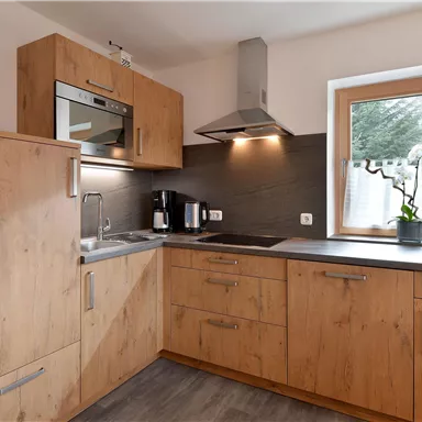 Eine moderne Küche mit Holzschränken und Edelstahlgeräten. Ein Fenster mit einer Pflanze sorgt für Tageslicht und eine einladende Atmosphäre.