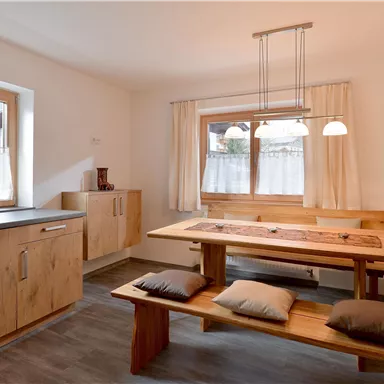 Eine moderne Küche mit Holzschränken und einer gemütlichen Essecke. Große Fenster lassen viel Licht herein.