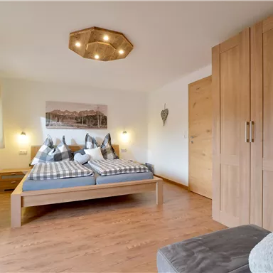 Ein modernes Schlafzimmer mit einem Doppelbett und Holzschrank. Das Zimmer hat helle Wände und große Fenster, die viel Licht hereinlassen.