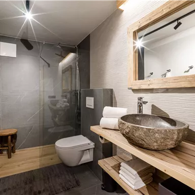 A modern bathroom with an elegant shower and a large mirror. The wooden shelves are stocked with towels and a decorative wash basin.