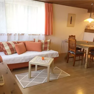 A cozy living space with a bright couch and a wooden dining table. Large windows provide plenty of light and an inviting atmosphere.