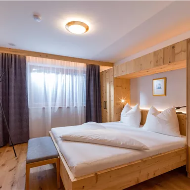 A cozy bedroom with wooden furniture and two beds. Bean curtains let in plenty of natural light.