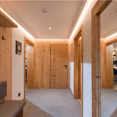 A modern hallway with wooden paneling and soft lighting. The doors lead to various rooms and create an inviting atmosphere.