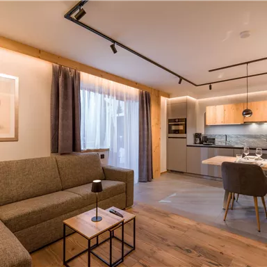 A modern living room with a cozy couch and a dining table. The kitchen is well-equipped and the light is warm and inviting.