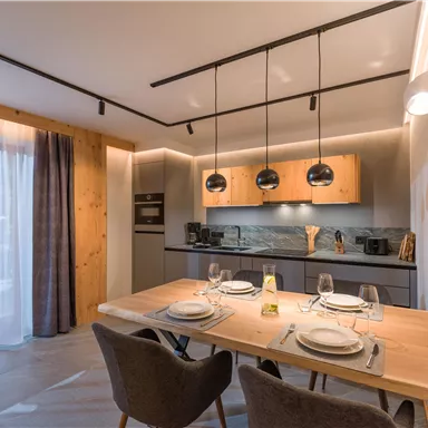 A modern kitchen with a dining area. The room features wooden details and stylish lighting.