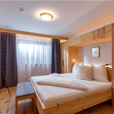 A modern bedroom with wooden paneling and a cozy bed. Large windows let in natural light and create an inviting atmosphere.