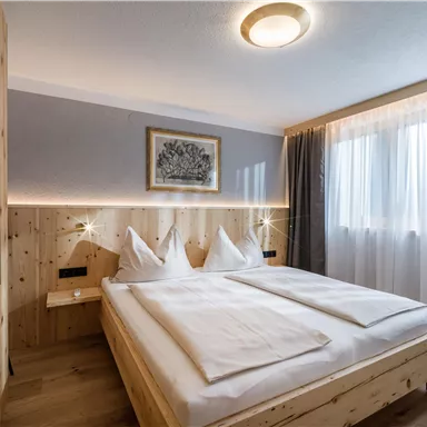 A modern bedroom with light wood and a large window. The bedding is white and the walls are softly painted gray.