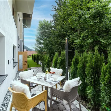 An inviting outdoor area with a table and chairs, surrounded by green hedges. The area is bright and friendly with a view of the garden.
