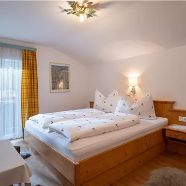 Ein gemütliches Schlafzimmer mit einem Doppelbett und Holzmöbeln. Große Fenster lassen viel Licht herein und sorgen für eine einladende Atmosphäre.