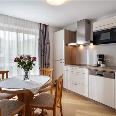 Eine moderne Küche mit einem runden Tisch und Holzstühlen. Auf dem Tisch steht eine Vase mit frischen Blumen.