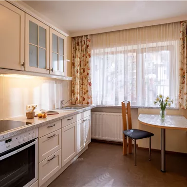 Eine helle Küche mit modernen Möbeln und einem großen Fenster. Der Tisch ist mit frischen Blumen dekoriert und es gibt platzierte Stühle.