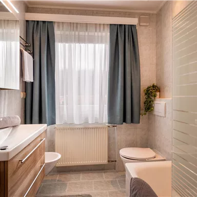 Ein modernes Badezimmer mit Holzdetails und weißen Wänden. Vorhänge in Blau und eine helle, einladende Atmosphäre.