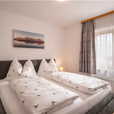 Ein gemütliches Schlafzimmer mit zwei Einzelbetten und hellen Vorhängen. An der Wand hängt ein Landschaftsbild, das die entspannende Atmosphäre unterstreicht.